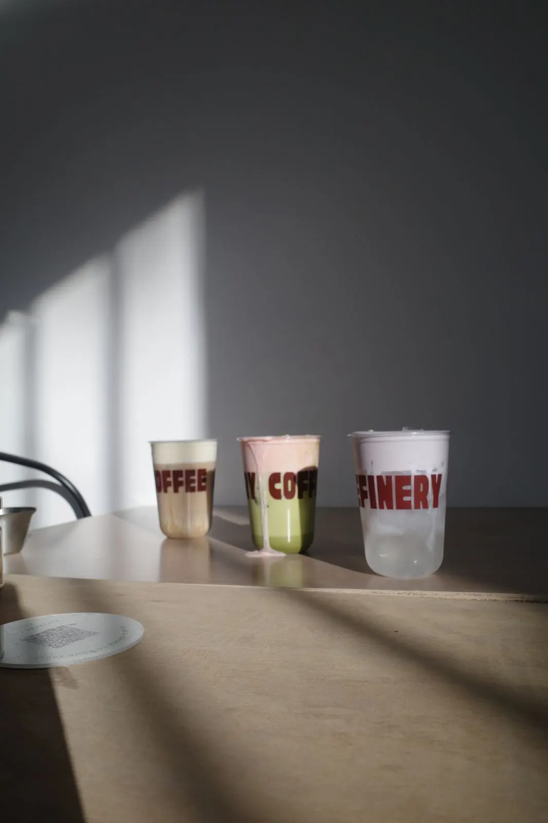 Three branded Refinery Coffee cups in dramatic window light
