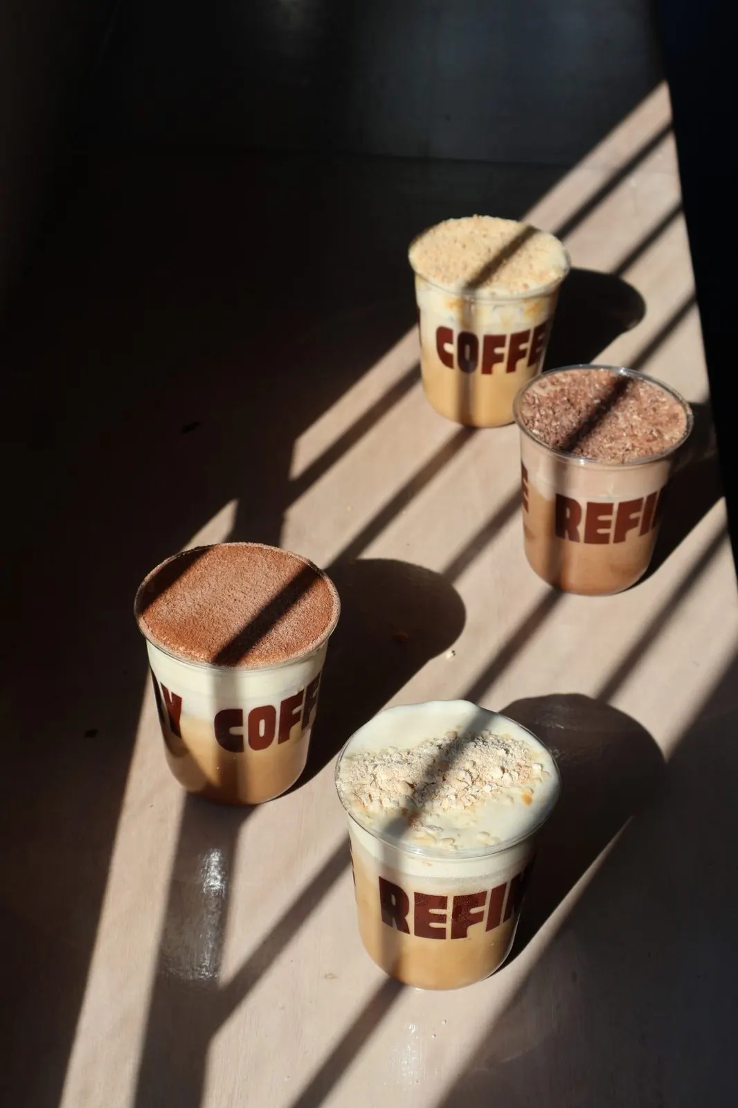 Four Refinery iced coffees topped with crumble in hard window light